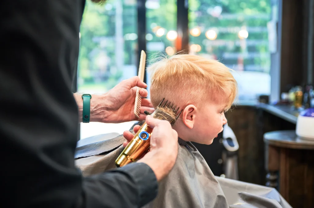 Professional hairdresser shaving little kid's nape