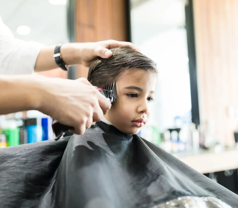 Boy having his hair trimmed by hairdresser in a barber shop