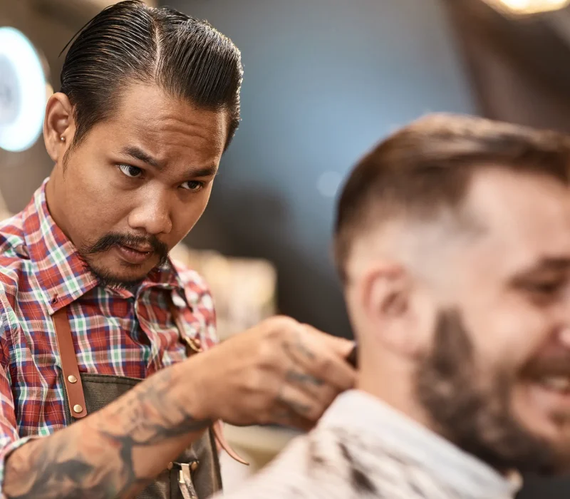 Serious professional hairdresser doing a haircut for a positive bearded man