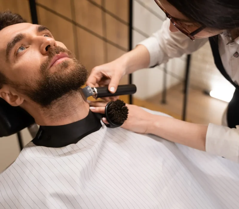 Woman cuts a beard of a male customer